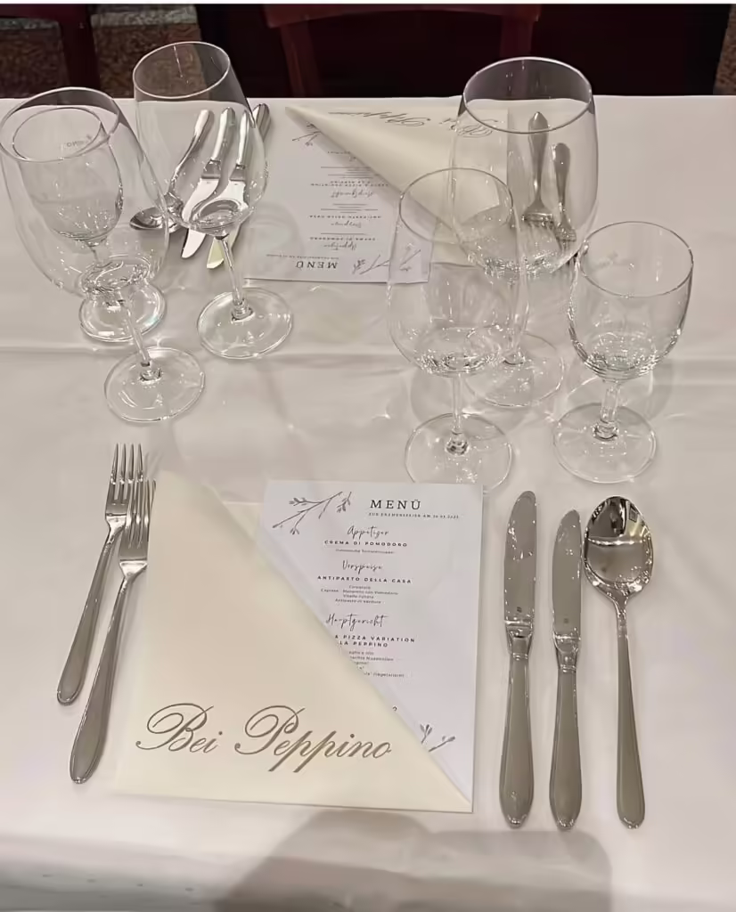 Elegantes Gedeck bei Peppino in Würzburg mit Menükarten, Weingläsern und Besteck auf weißer Tischdecke für Feierlichkeiten