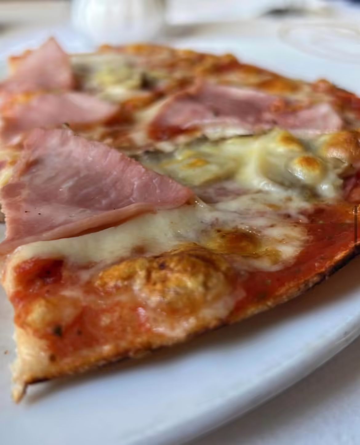 Dünnes Stück Pizza Peppino mit geschmolzenem Käse, Tomatensauce und Schinken auf weißem Teller im Restaurant Bei Peppino